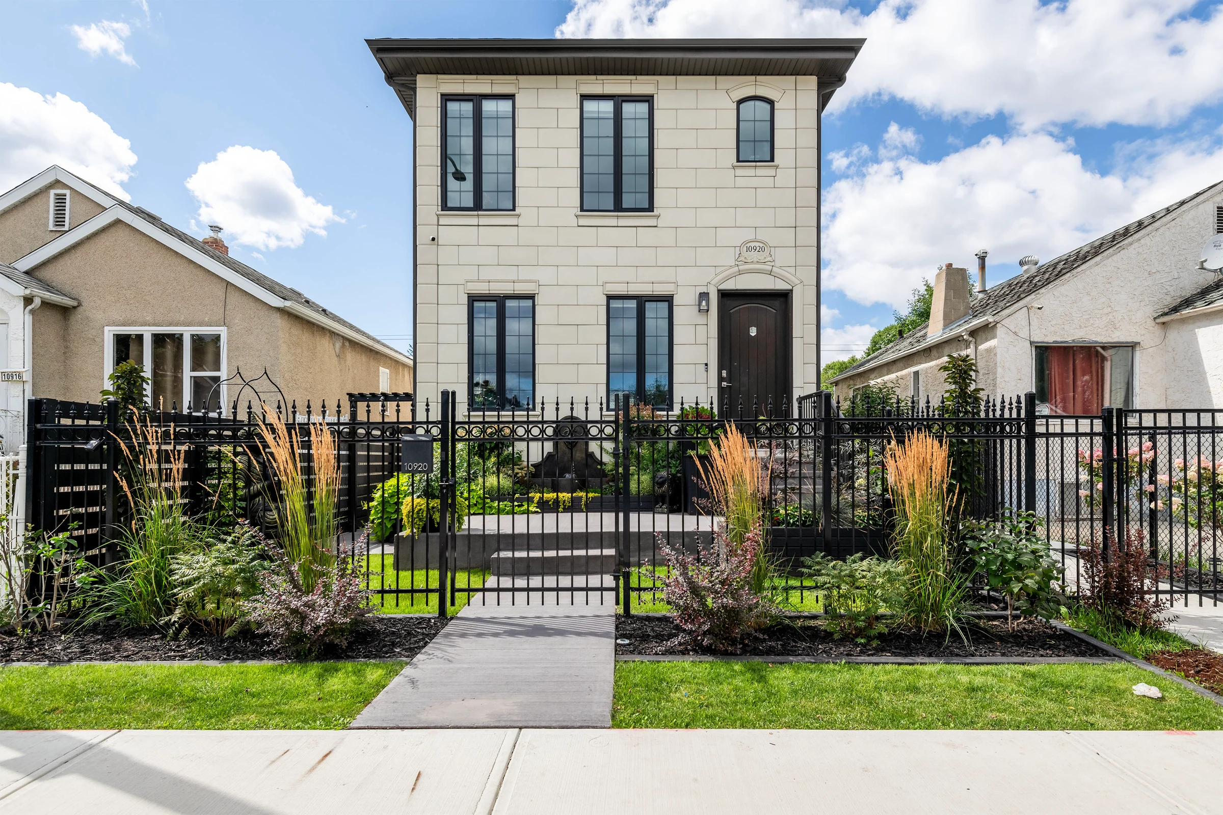 Front exterior of 10920 Church Street with cast-stone facade, black fence, and summer garden